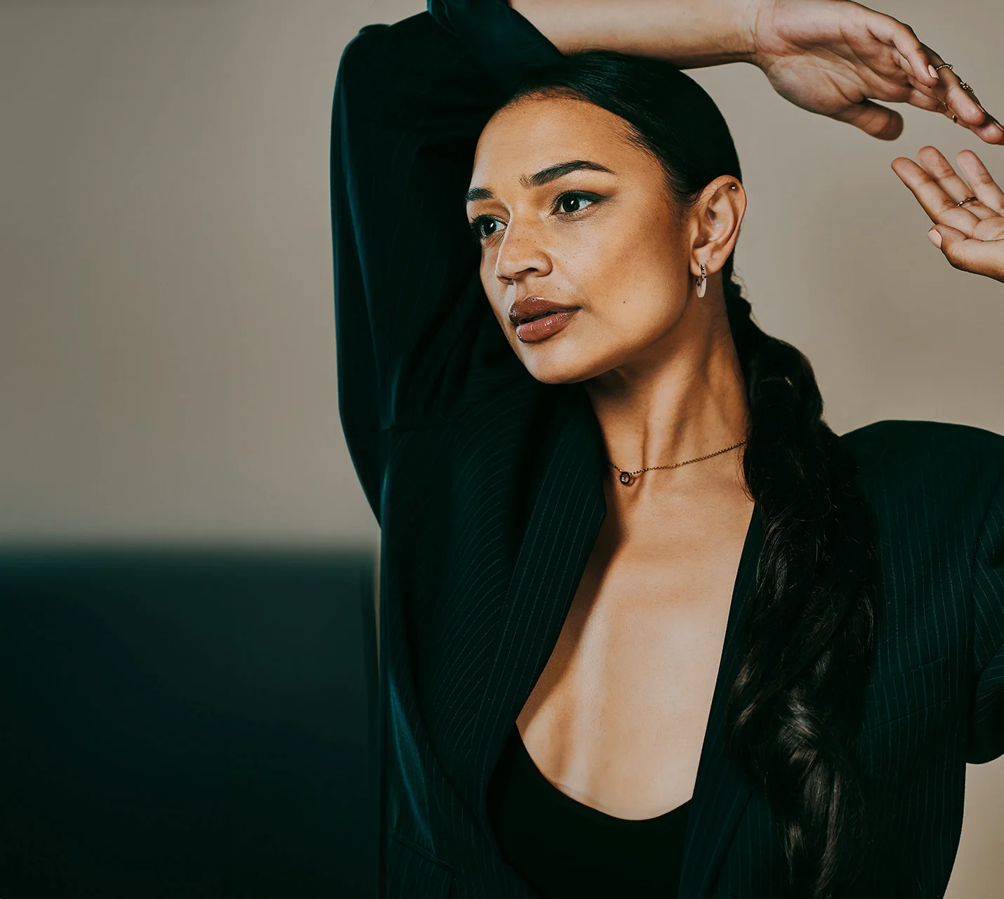 A woman with long, dark hair poses in a black blazer, arms raised, showcasing a confident and elegant expression. - Breast Implant Illness in West Village, New York, NY