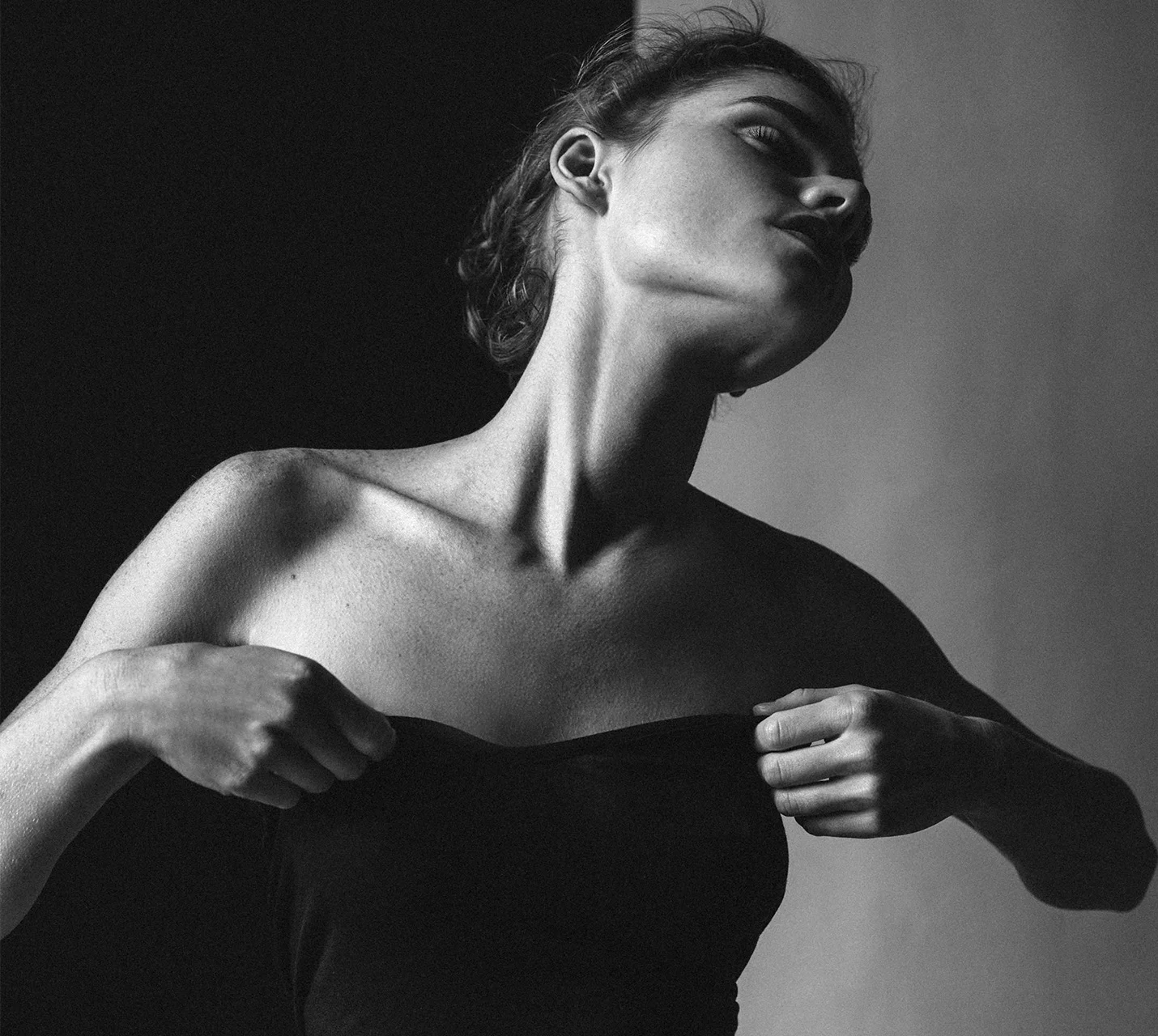A poised person in a black strapless top tilts their head, showcasing strong neck lines against a contrasting background. - Breast Reduction in West Village, New York, NY