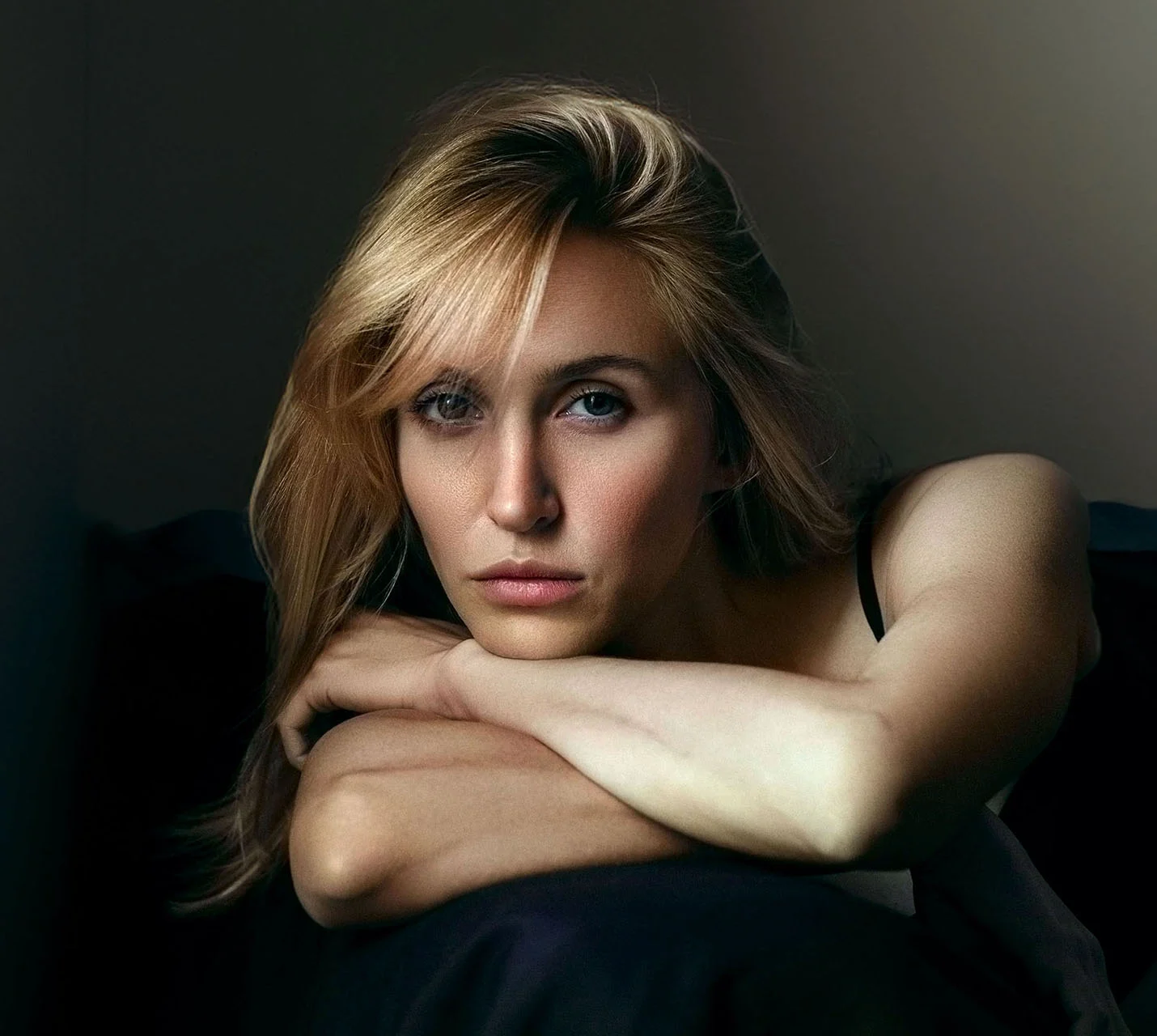 A close-up of a woman with blonde hair, resting her arms on a dark surface, gazing thoughtfully into the distance. - Face Lift in West Village, New York, NY