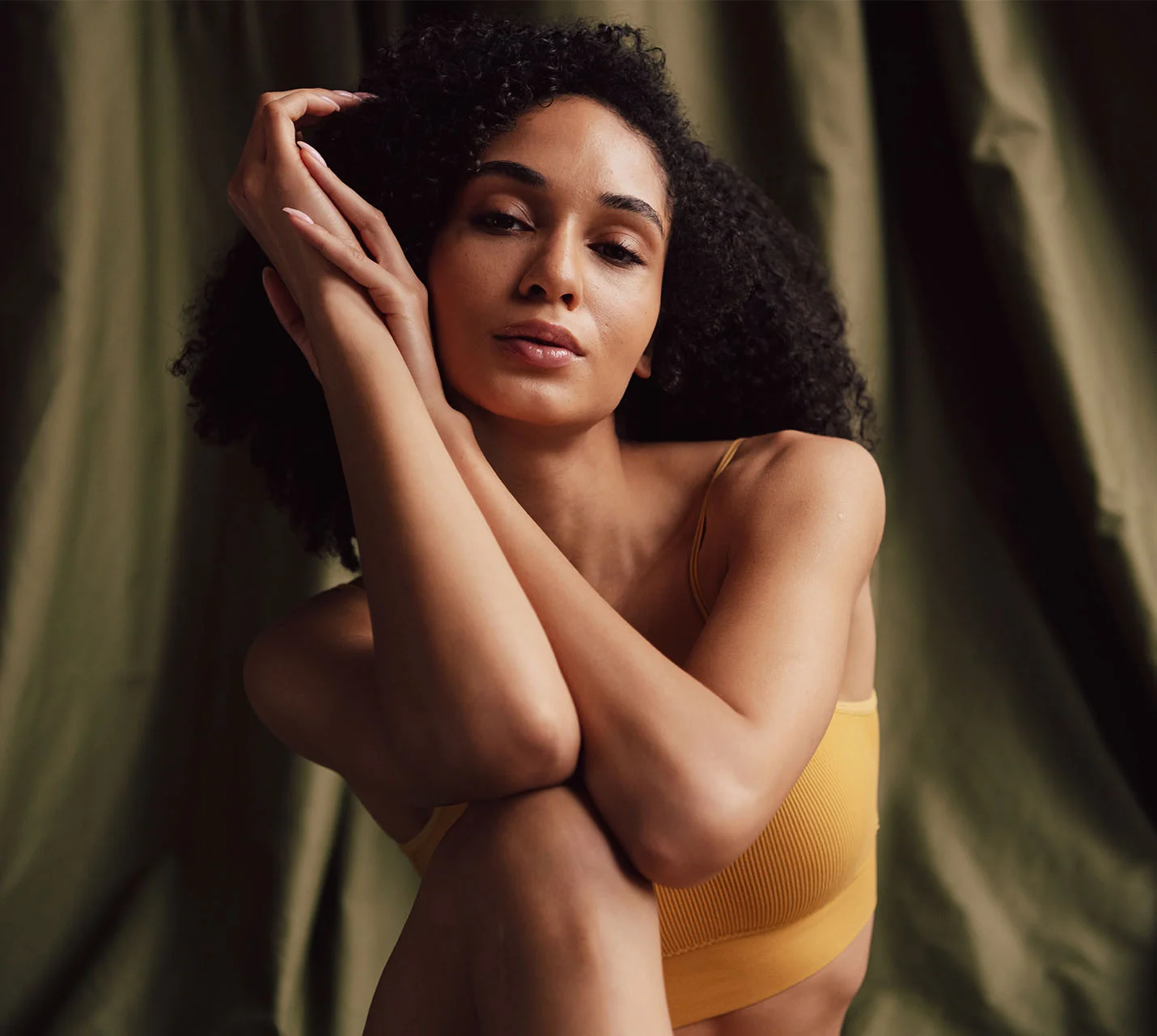 A woman with curly hair sits against a green backdrop, wearing a yellow top, with a gentle expression and crossed arms. - MOHS Reconstruction in West Village, New York, NY