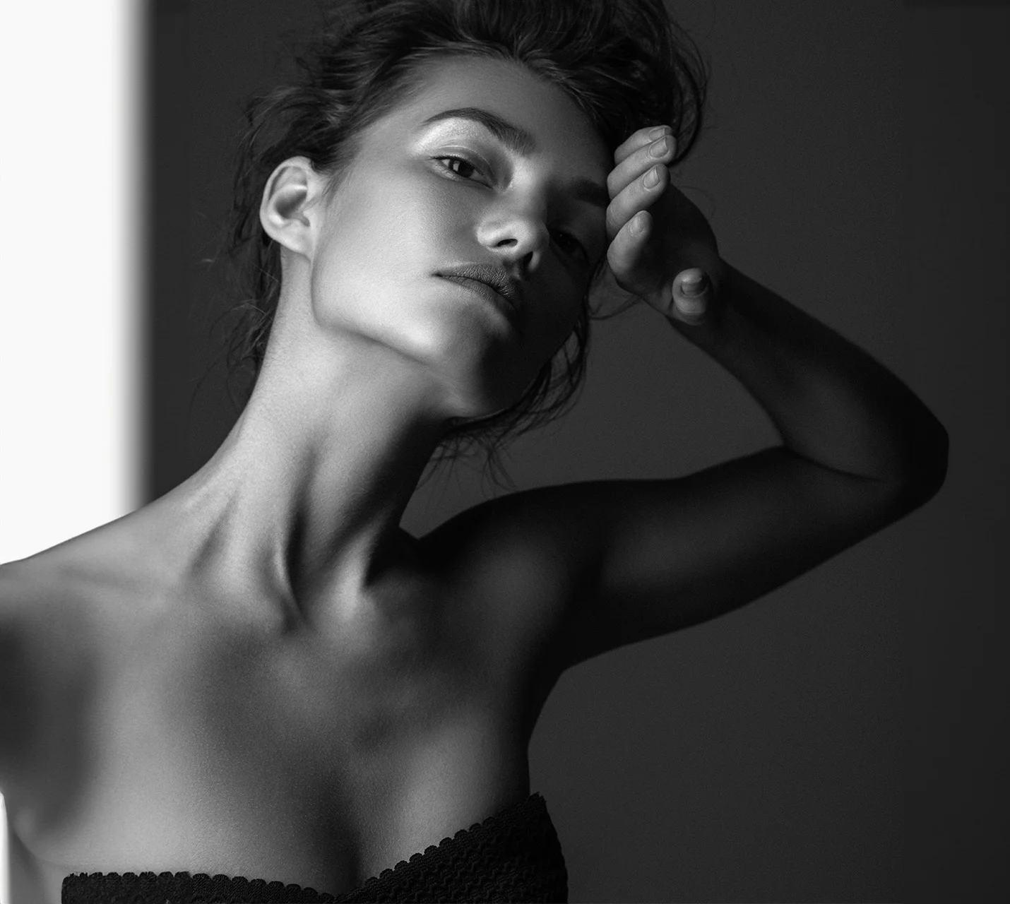 A woman in a black strapless top poses elegantly, with her hand on her head, against a contrasting dark background. - Neck Liposuction in West Village, New York, NY