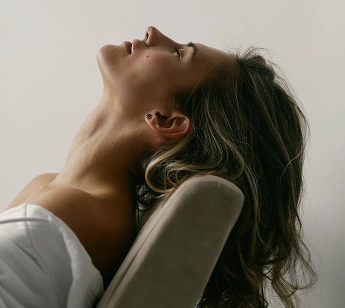 A woman with long, wavy hair leans back against a soft surface, eyes closed, exuding a peaceful, contemplative expression. - Neck Lift in West Village, New York, NY