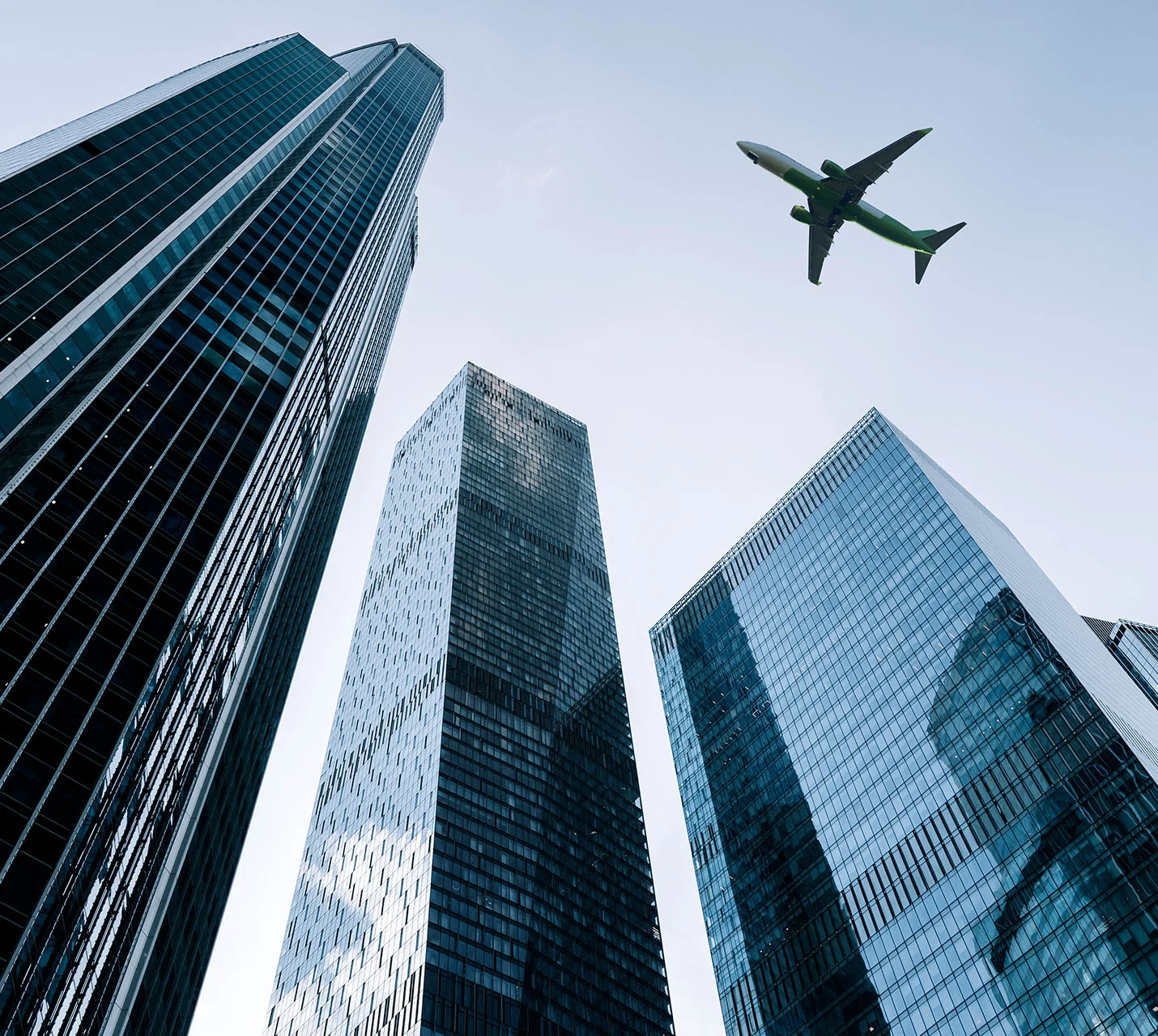 A low-angle view of tall skyscrapers with a plane flying above against a clear sky, reflecting in glass surfaces. - Out of Town in West Village, New York, NY