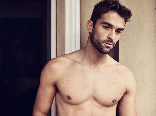 A young man with a well-defined physique stands shirtless against a neutral background, looking thoughtfully at the camera. - Men's Gynecomastia in West Village, New York, NY