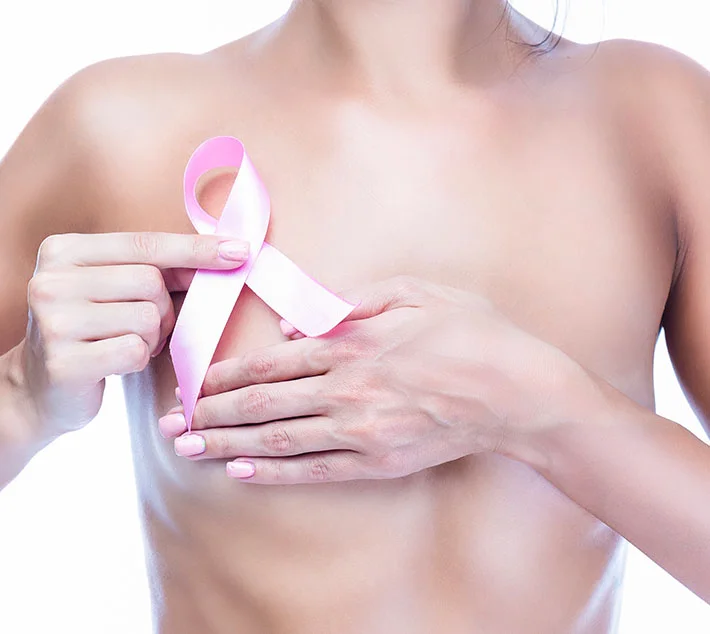 A close-up of a woman’s torso holding a pink breast cancer awareness ribbon against her chest. - Breast Cancer Reconstruction in West Village, New York, NY