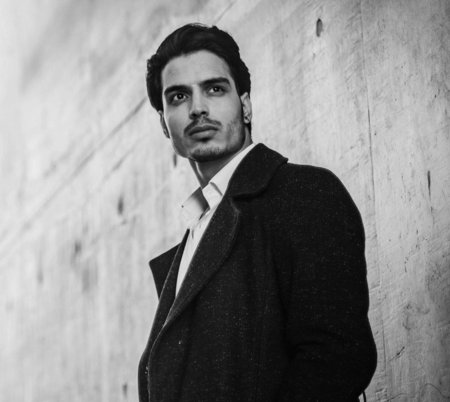 A stylishly dressed man gazes thoughtfully, leaning against a textured wall, captured in a black and white photo. - The Male Aesthetic in West Village, New York, NY